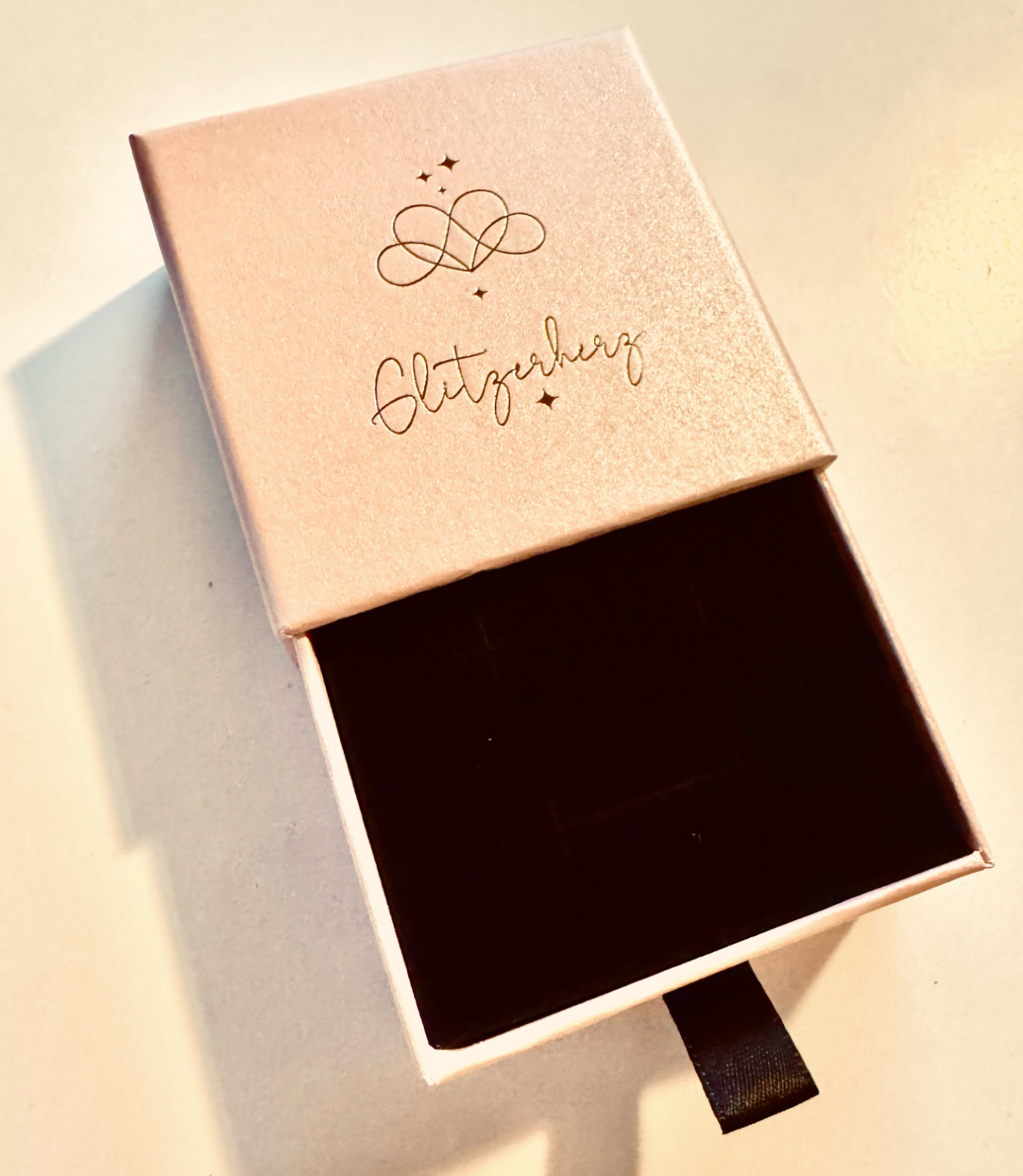 Eine geöffnete Schmuckschatulle mit schwarzer Innenfläche und einem Schriftzug.